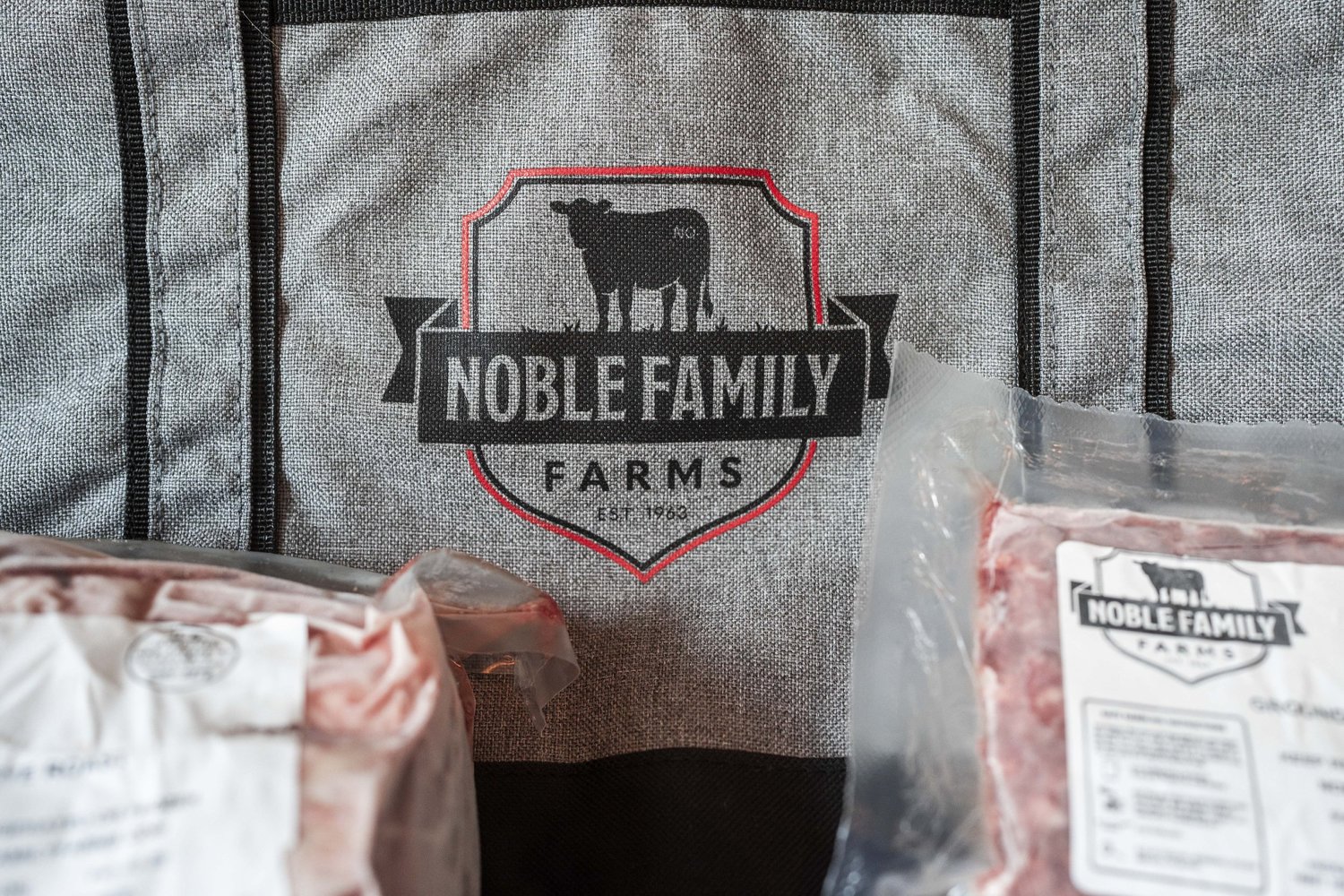 Noble Family Farms logo on a gray tote bag with packaged meat products, highlighting quality and farm-fresh offerings.