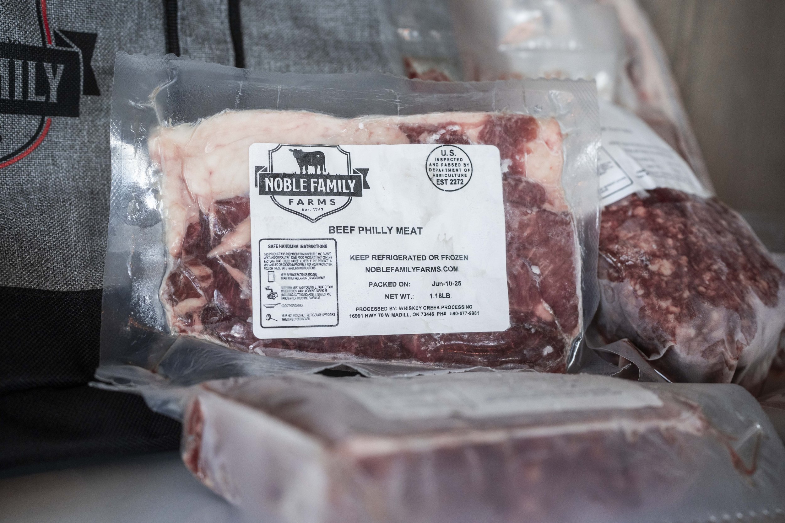 Packaging of Noble Family Farms Beef Philly Meat, featuring clear labeling with safe handling instructions, weight of 1.81 lbs, and a packing date of June 10, 2025, set against a backdrop of additional meat packages.
